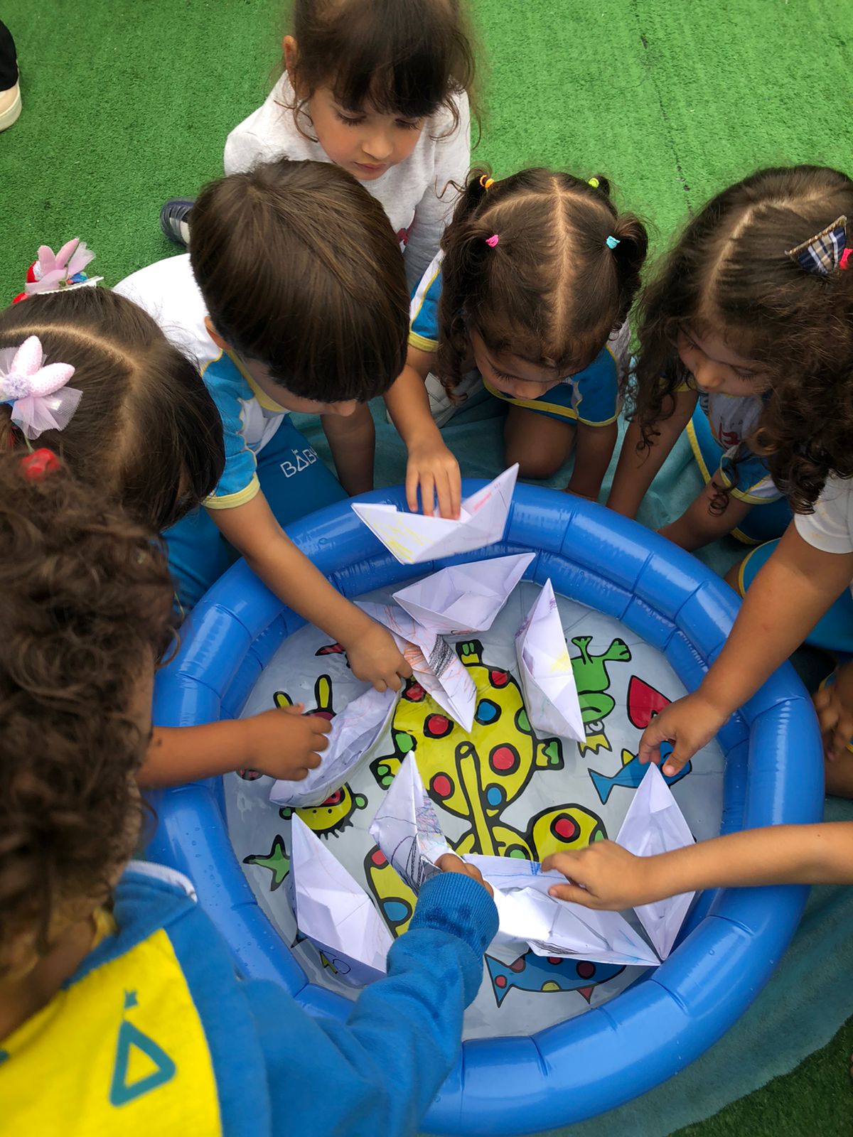 Crianças da Espaço Baby brincando juntas com barquinhos de papel no pátio